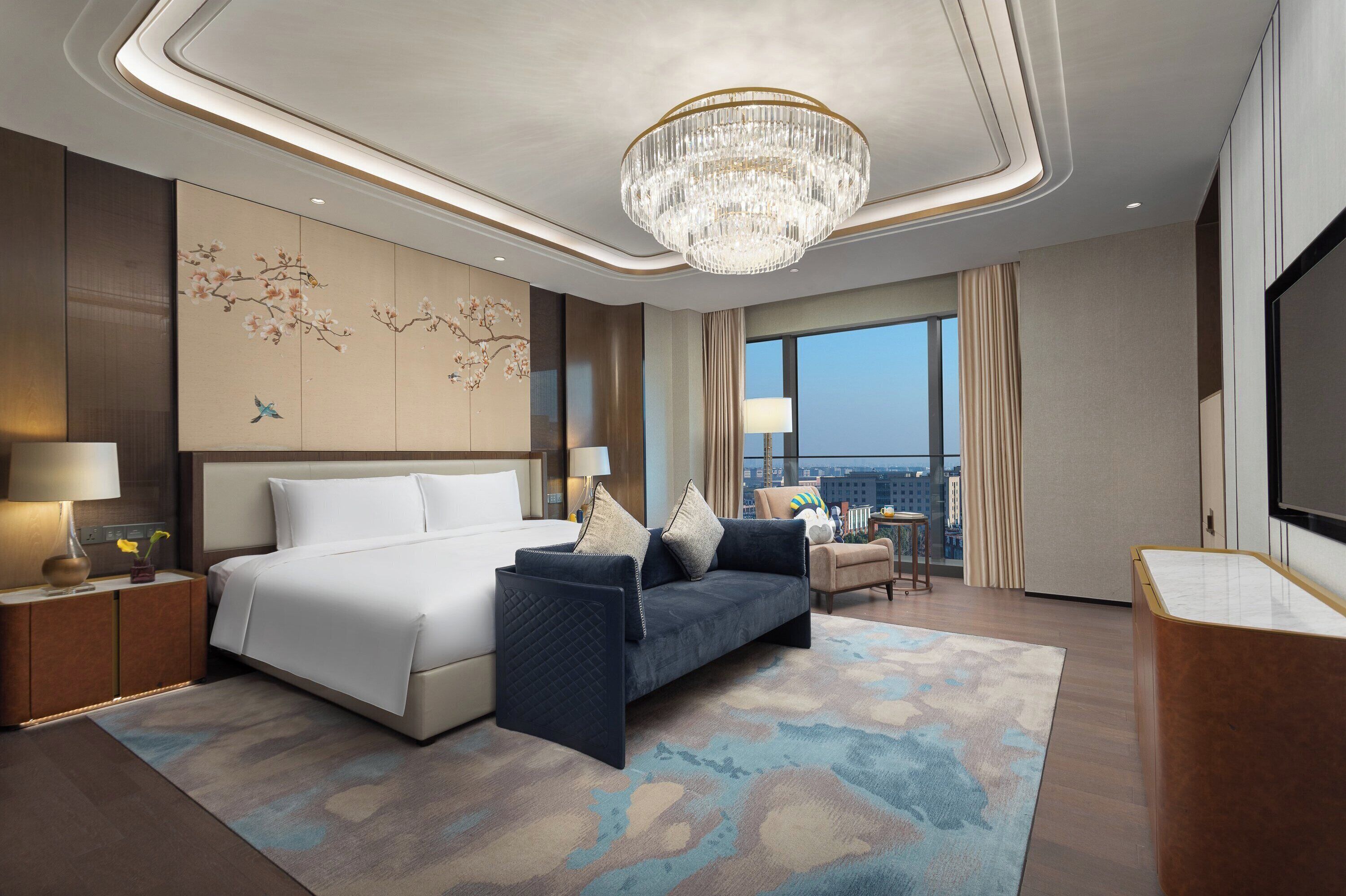 Een moderne hotelkamer met een groot bed, een bank, een bureau en een kroonluchter.