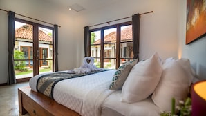 A bedroom with a large bed, a wooden bench, and a view of a courtyard through open doors. - The Georgina Estate (Nusa Dua)