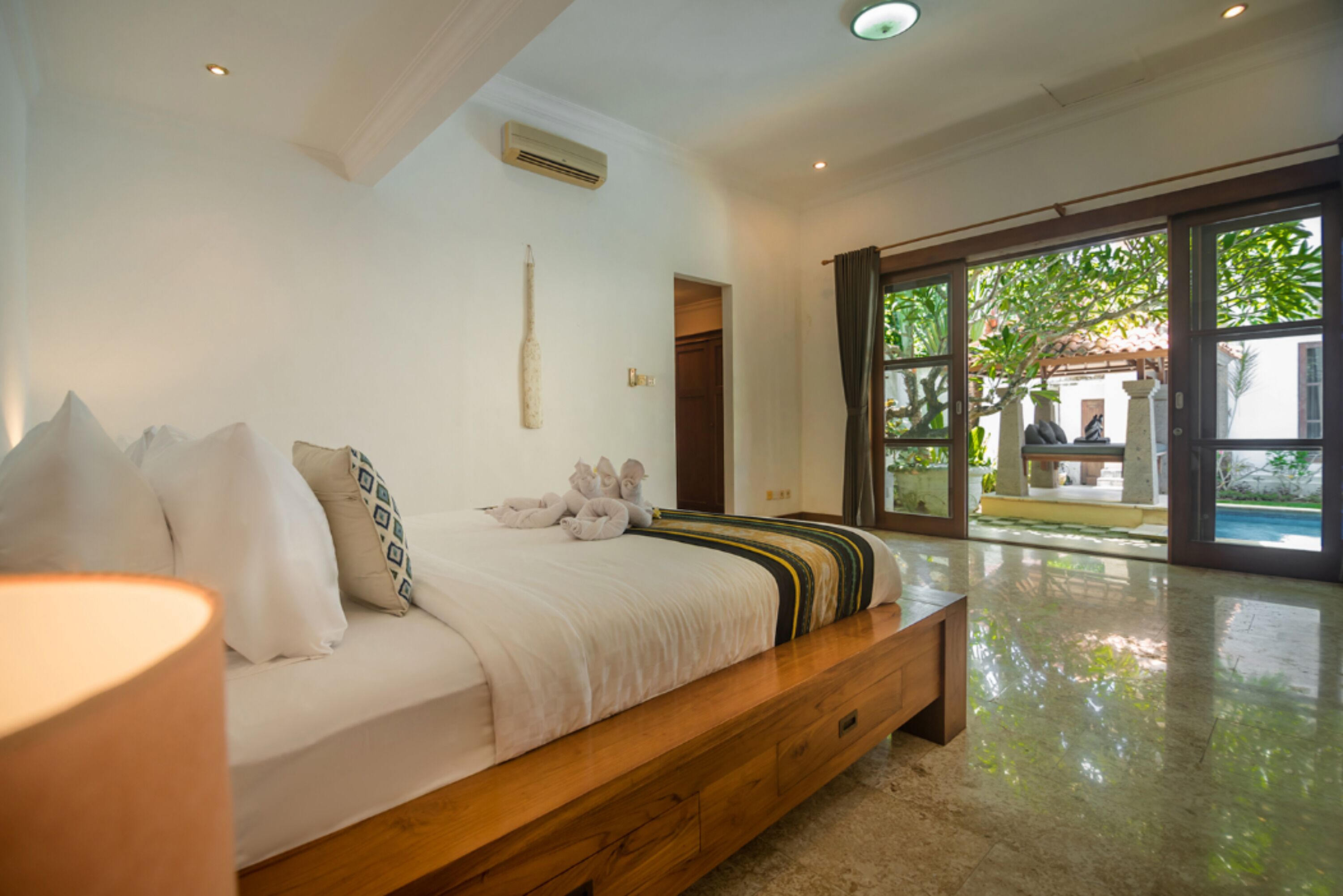 Un dormitorio con cama de madera, ropa de cama blanca y un ventanal con vistas al exterior.