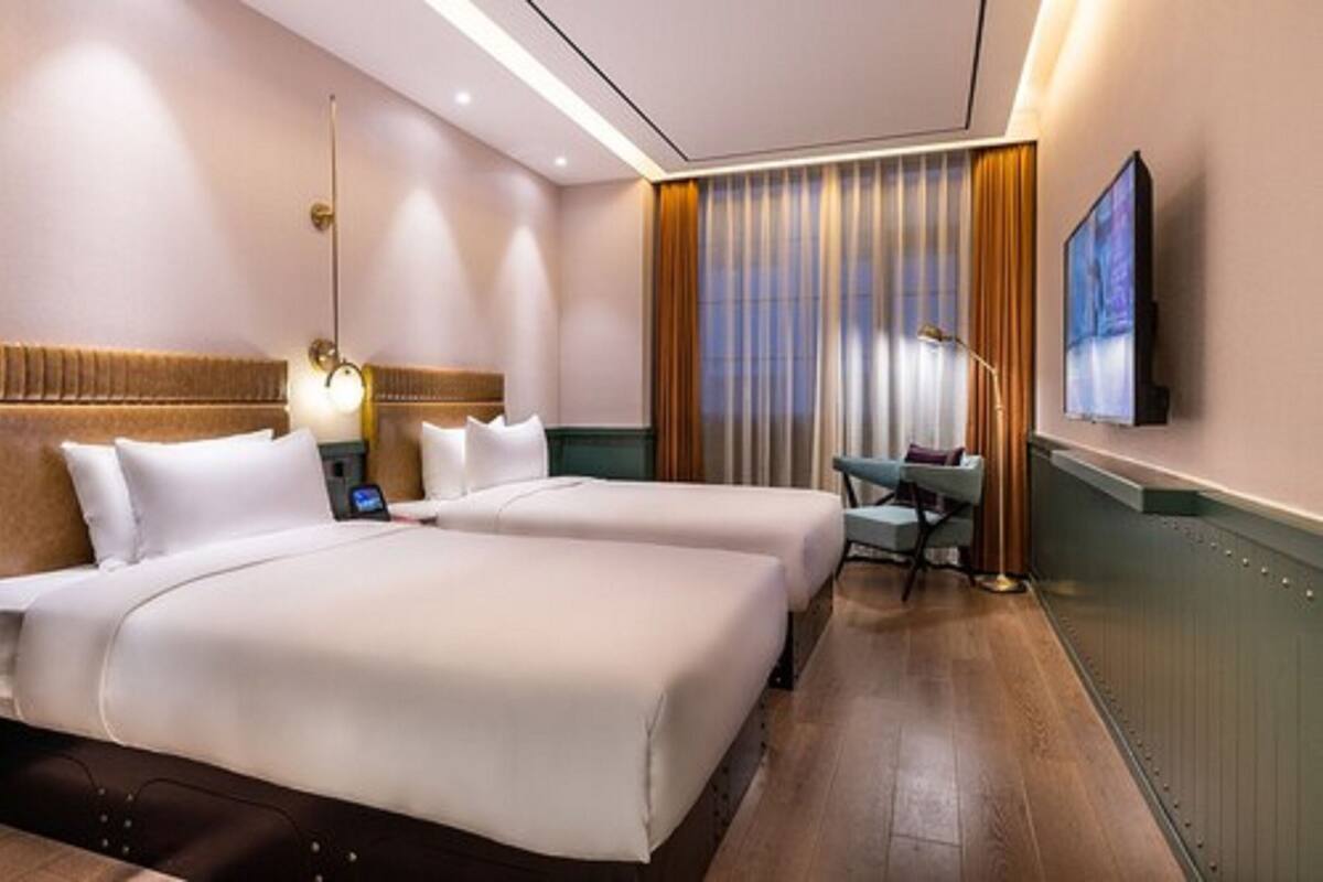 A hotel room with two beds, a desk, a chair, a TV, and a window with curtains.