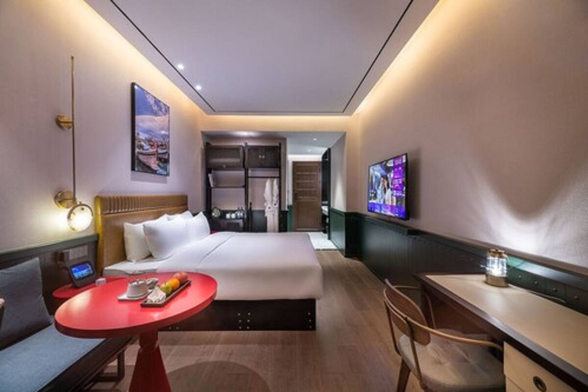A hotel room with a bed, a desk, a TV, a red table, and a wardrobe.