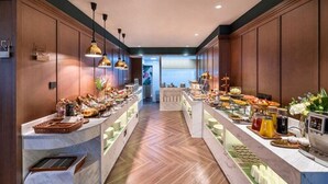 Zona de bufé con diversas opciones de comida y bebidas, paneles de madera e iluminación colgante.