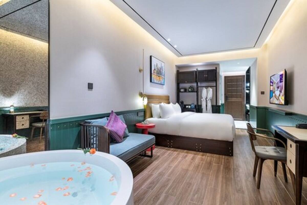 A hotel room with a bed, a desk, a chair, a small table, a sofa, a bathtub with rose petals, and a mirror.