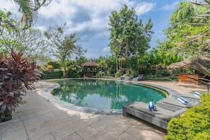 A swimming pool with lounge chairs and a gazebo surrounded by tropical plants.