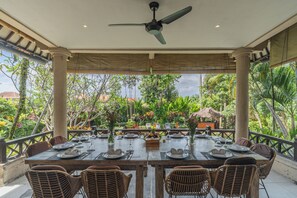 An outdoor dining area with a table set for four, surrounded by wicker chairs, under a ceiling fan.