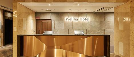 Uma receção com design moderno, um letreiro indicando "Welina Hotel" e um chão com padrão losango.