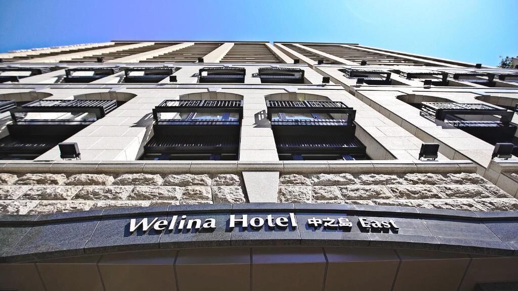 The exterior of the Welina Hotel with a modern architectural design, featuring large windows and a prominent signage.