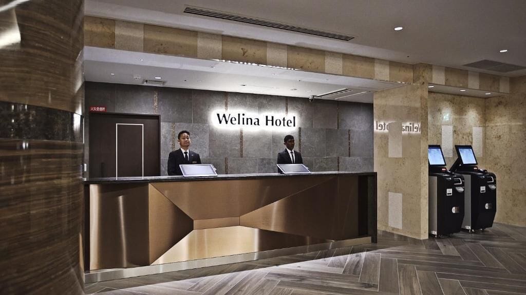 Bancada de recepção no Hotel Welina com dois funcionários, design moderno e espaço para guardar bagagem.