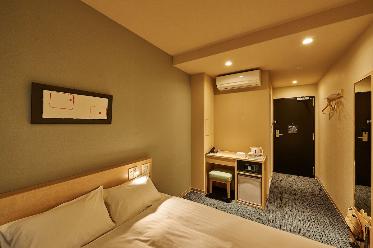 Une chambre d’hôtel équipée d’un lit, d’un bureau, d’une chaise, d’une petite poubelle et d’un appareil de climatisation.