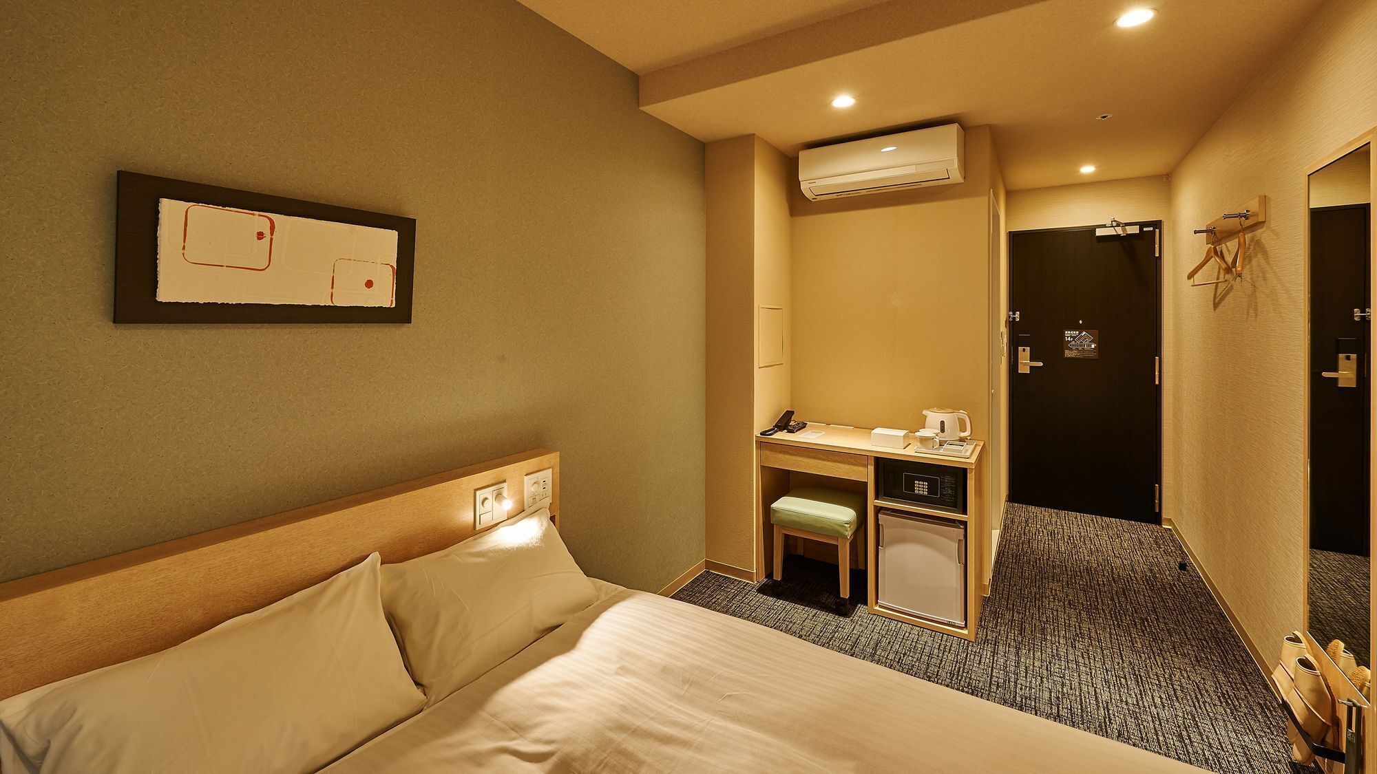 Une chambre d’hôtel comprenant un lit, un bureau avec un téléphone et une machine à café, un appareil de climatisation et une porte.