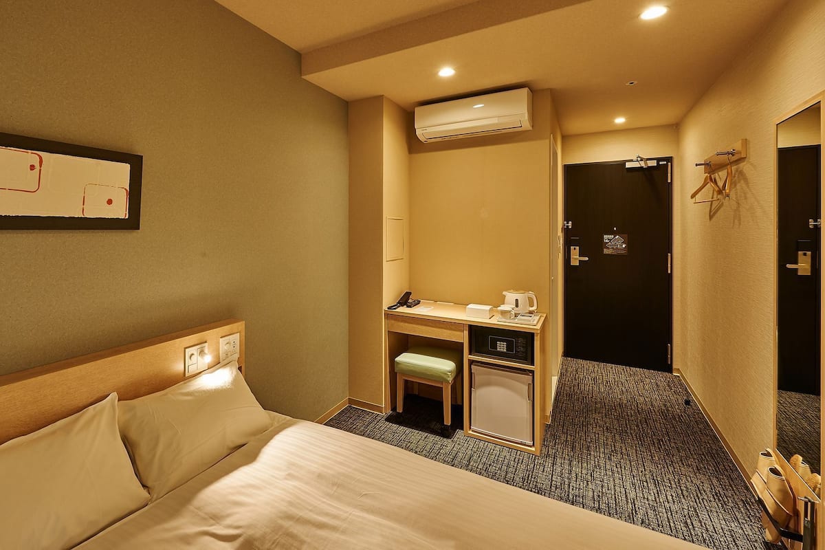 Une chambre d’hôtel comprenant un lit, un bureau avec un téléphone et une machine à café, un appareil de climatisation et une porte.