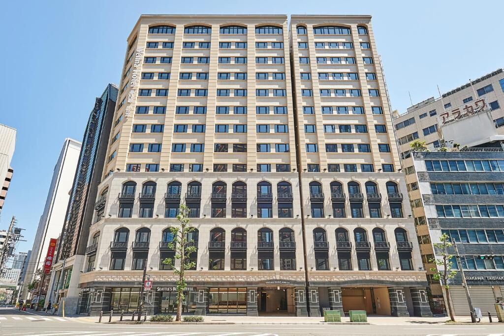 A multi-story hotel with a classic architectural design, featuring a central entrance with large windows and a ground-level retail space.