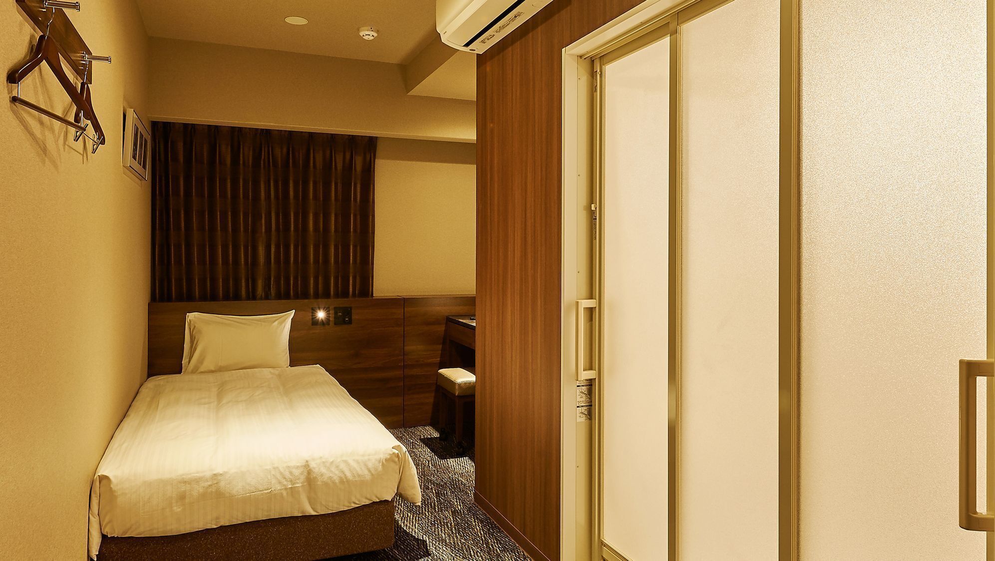 Une chambre d’hôtel avec un lit, un bureau, une chaise, une armoire et un rideau.