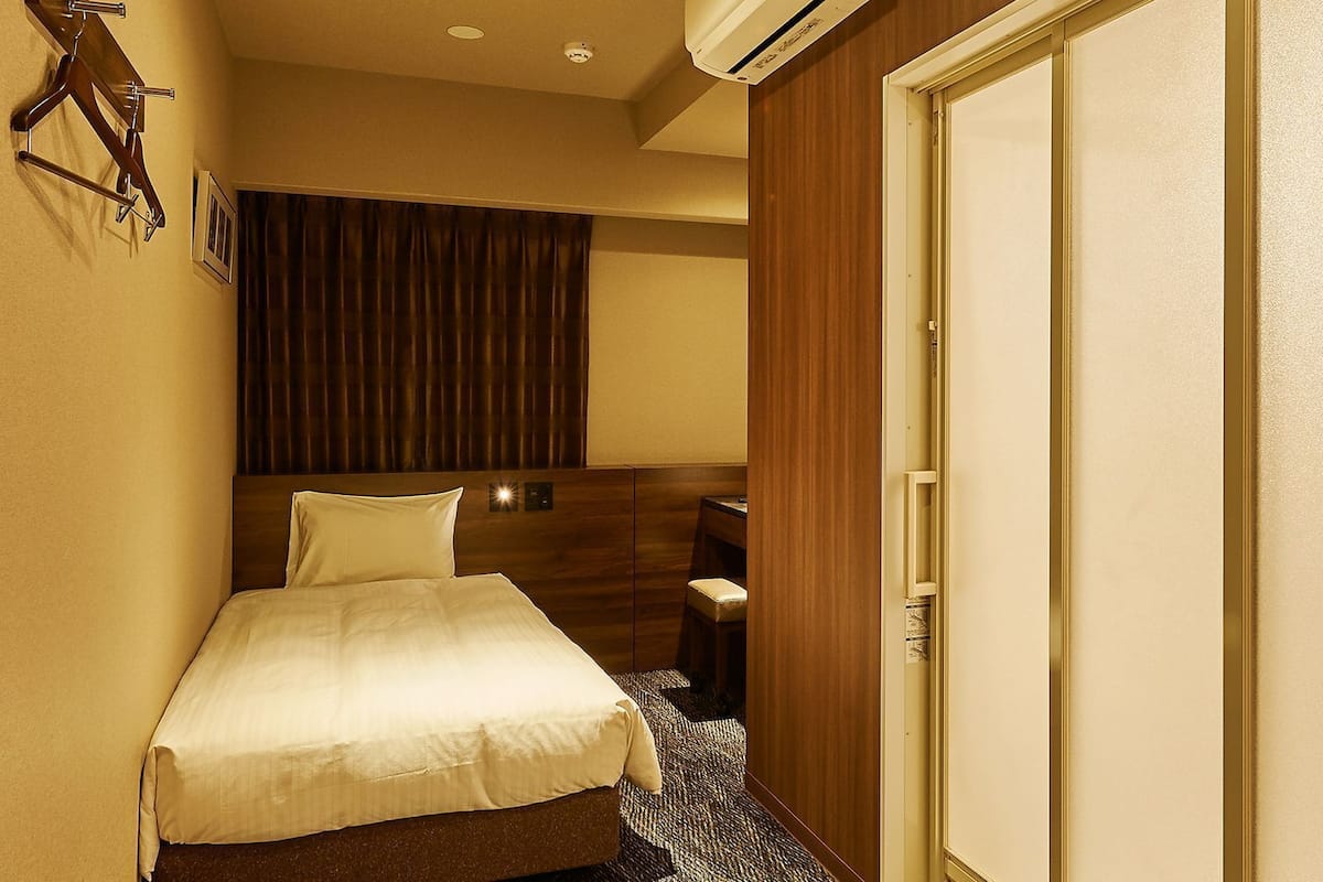 Une chambre d’hôtel avec un lit, un bureau, une chaise, une armoire et un rideau.