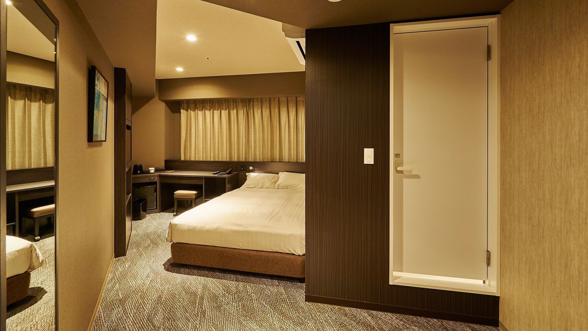 Une chambre d’hôtel avec un lit, un bureau, une chaise et une porte.