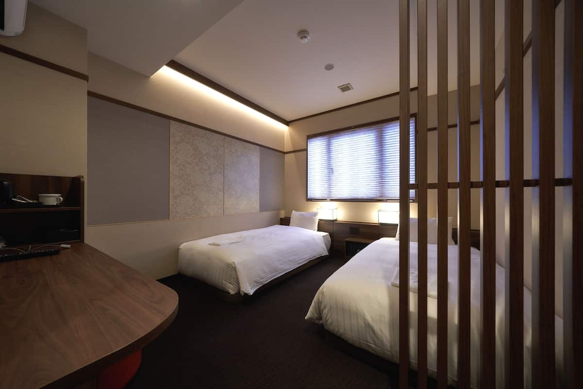 Ein Hotelzimmer mit zwei Betten, einem Schreibtisch und einem Fenster mit Jalousien.