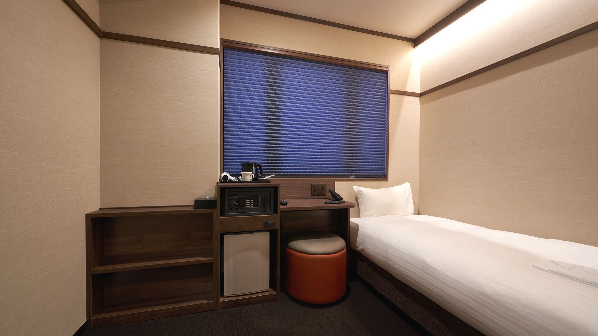 A hotel room with a bed, a small desk with a microwave, a telephone, and a trash bin.