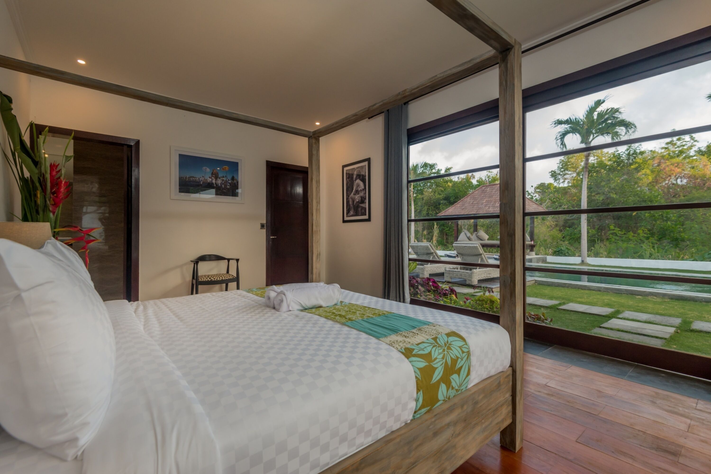 A bedroom with a large bed, a view of a garden through a sliding glass door, and a framed picture on the wall.
