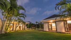 A modern villa with large glass windows, a well-maintained lawn, and palm trees.