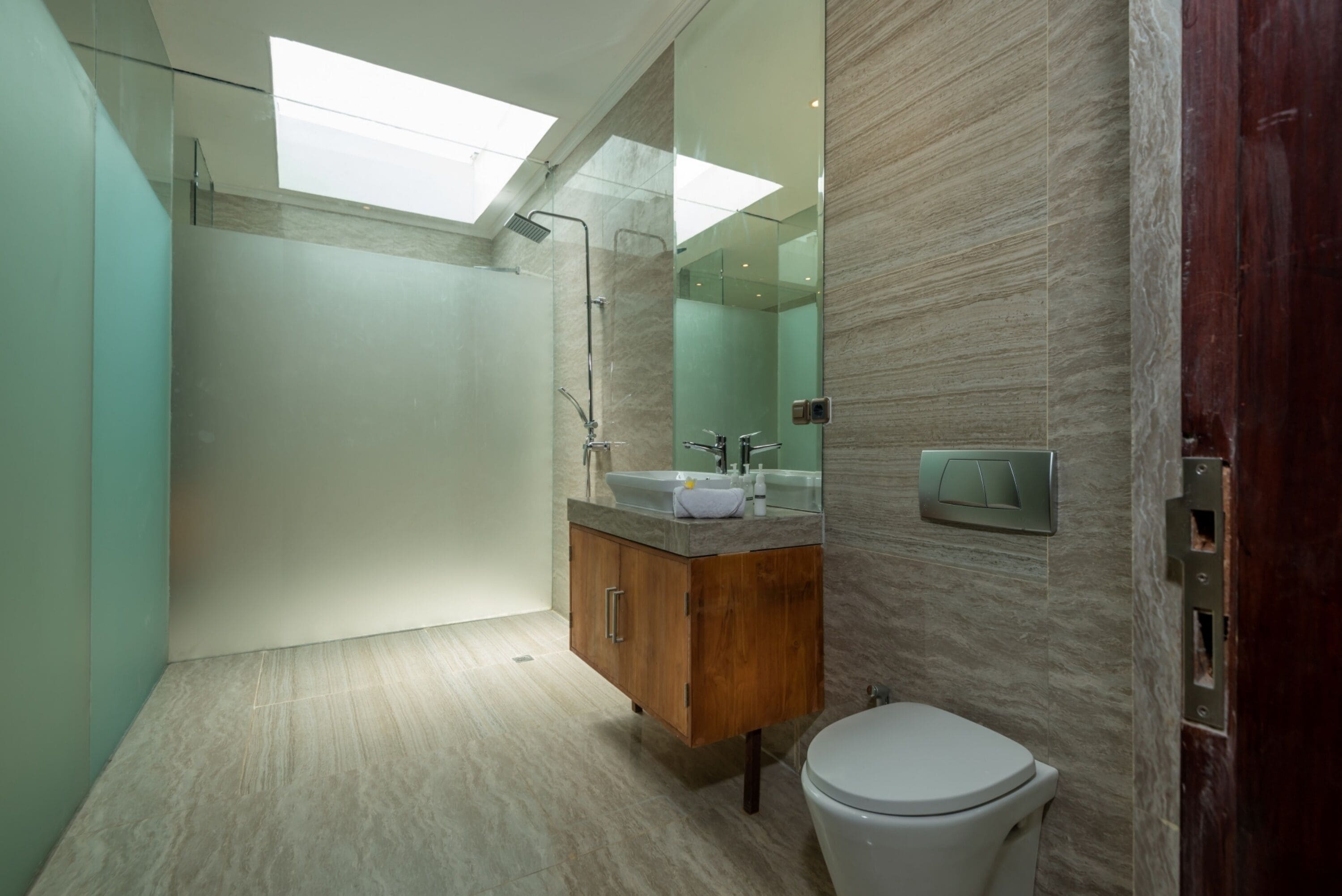 A modern bathroom with a skylight, a wooden vanity, a white toilet, and a glass shower enclosure.