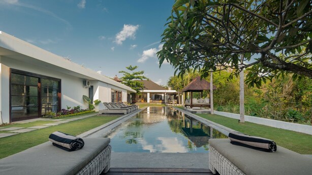 A modern pool area with two lounge chairs and a pathway leading to a house.