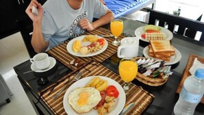 A breakfast table with plates of eggs, toast, and fruit, a coffee cup, and a water bottle.