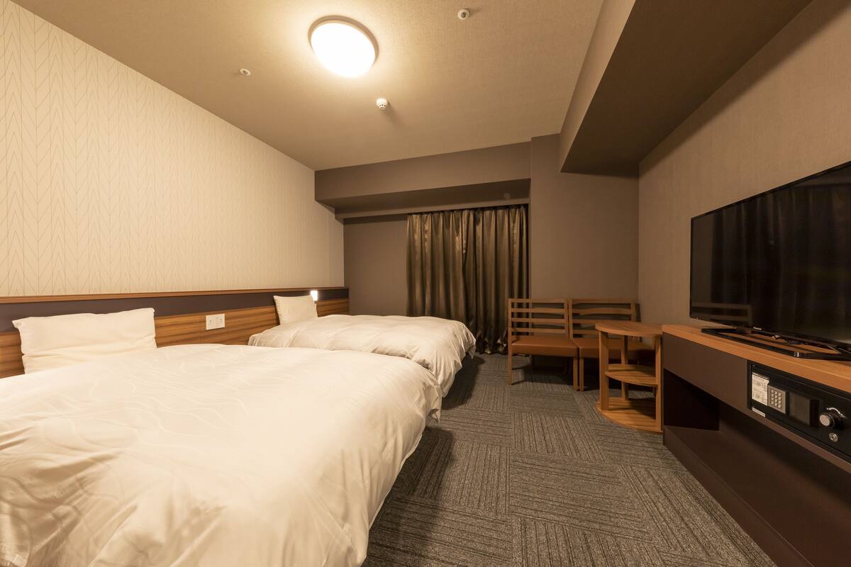 A hotel room with two beds, a TV, a desk, and a chair.