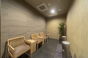 Un área de espera con bancos y sillas de madera, un cubo de basura y una planta en maceta.