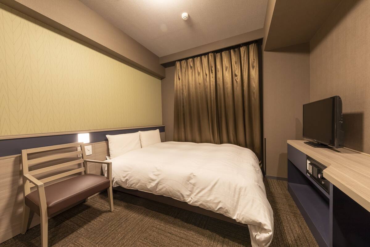 A hotel room with a bed, a wooden bench, a television, and a control panel.