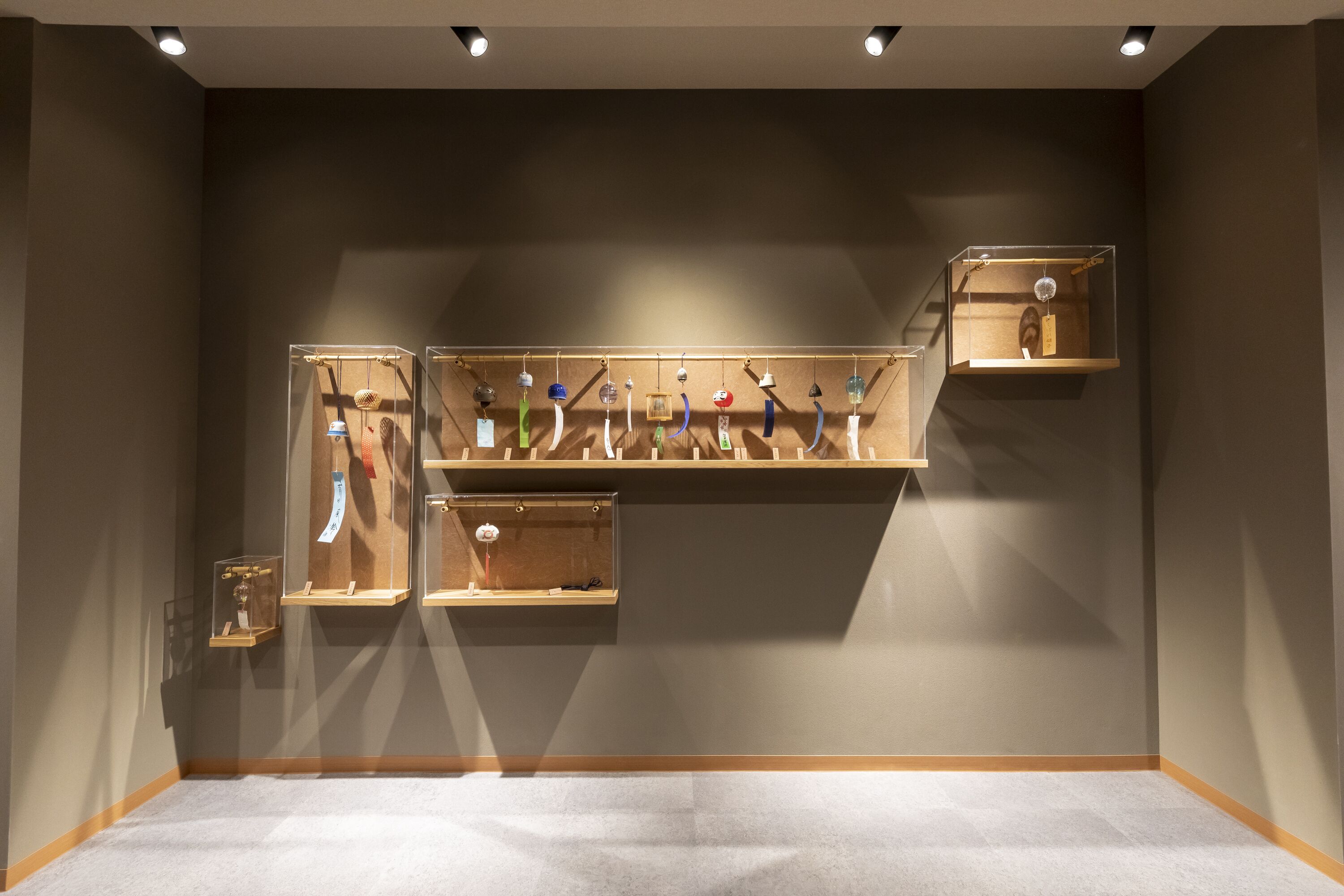 Una habitación con piso alfombrado, una repisa de madera con varios objetos, y una vitrina fijada a la pared.