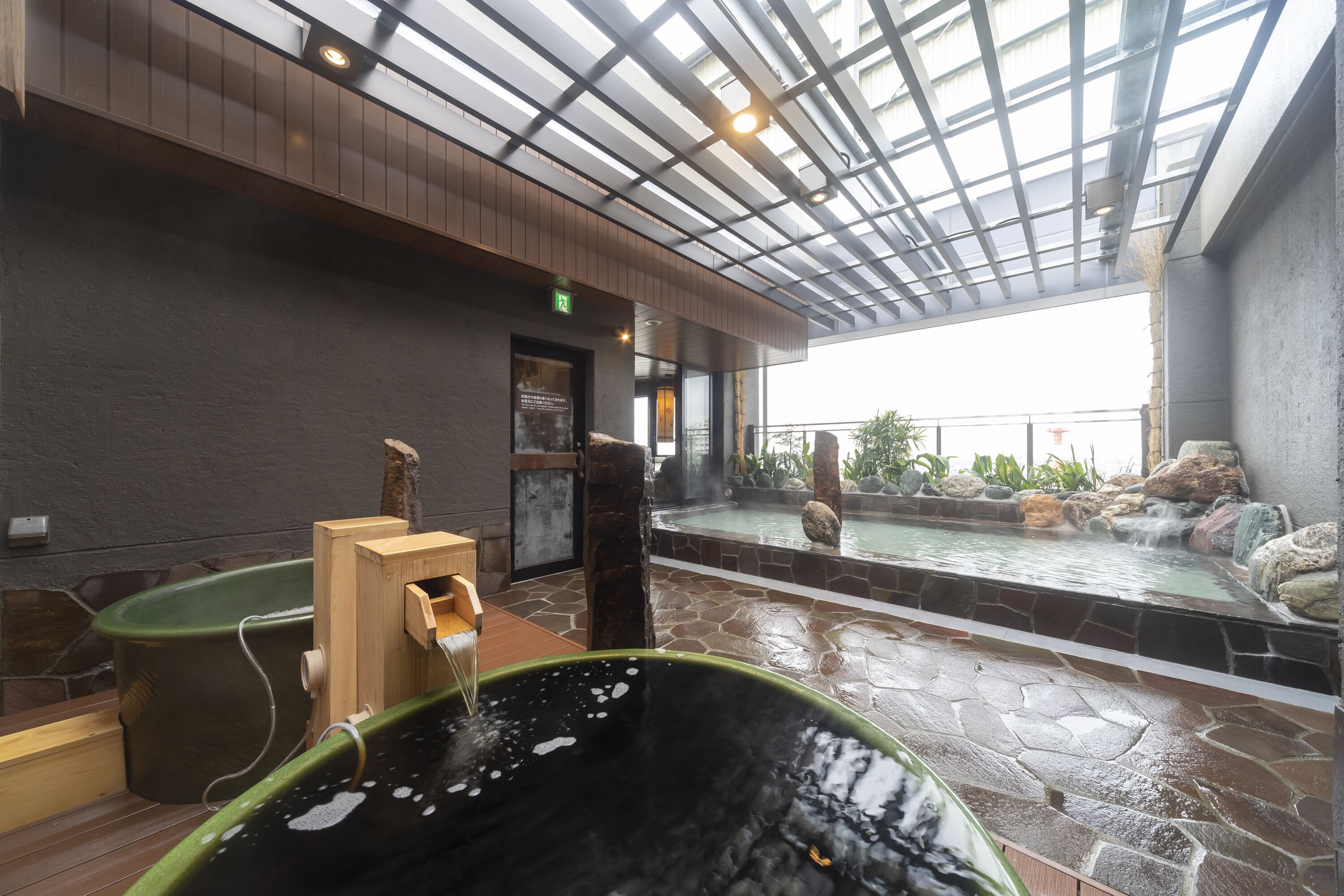 Een wellnessruimte met een bubbelbad, houten zitplaatsen en een vloer van stenen tegels.