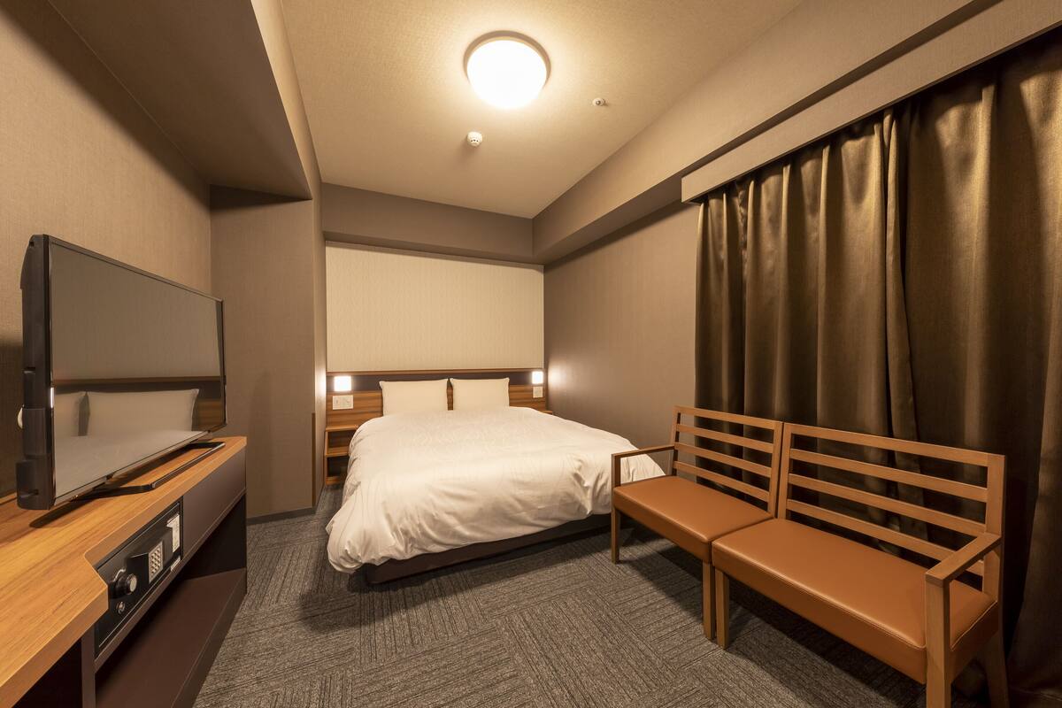 A hotel room with a bed, a TV, a bench, and a curtain.