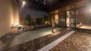 A stone hot tub area with a wooden deck, a stone wall, and a glass enclosure. - Dormy Inn Kawasaki Natural Hot Spring (Kawasaki)