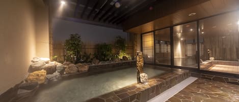 A stone hot tub area with a wooden deck, a stone wall, and a glass enclosure.