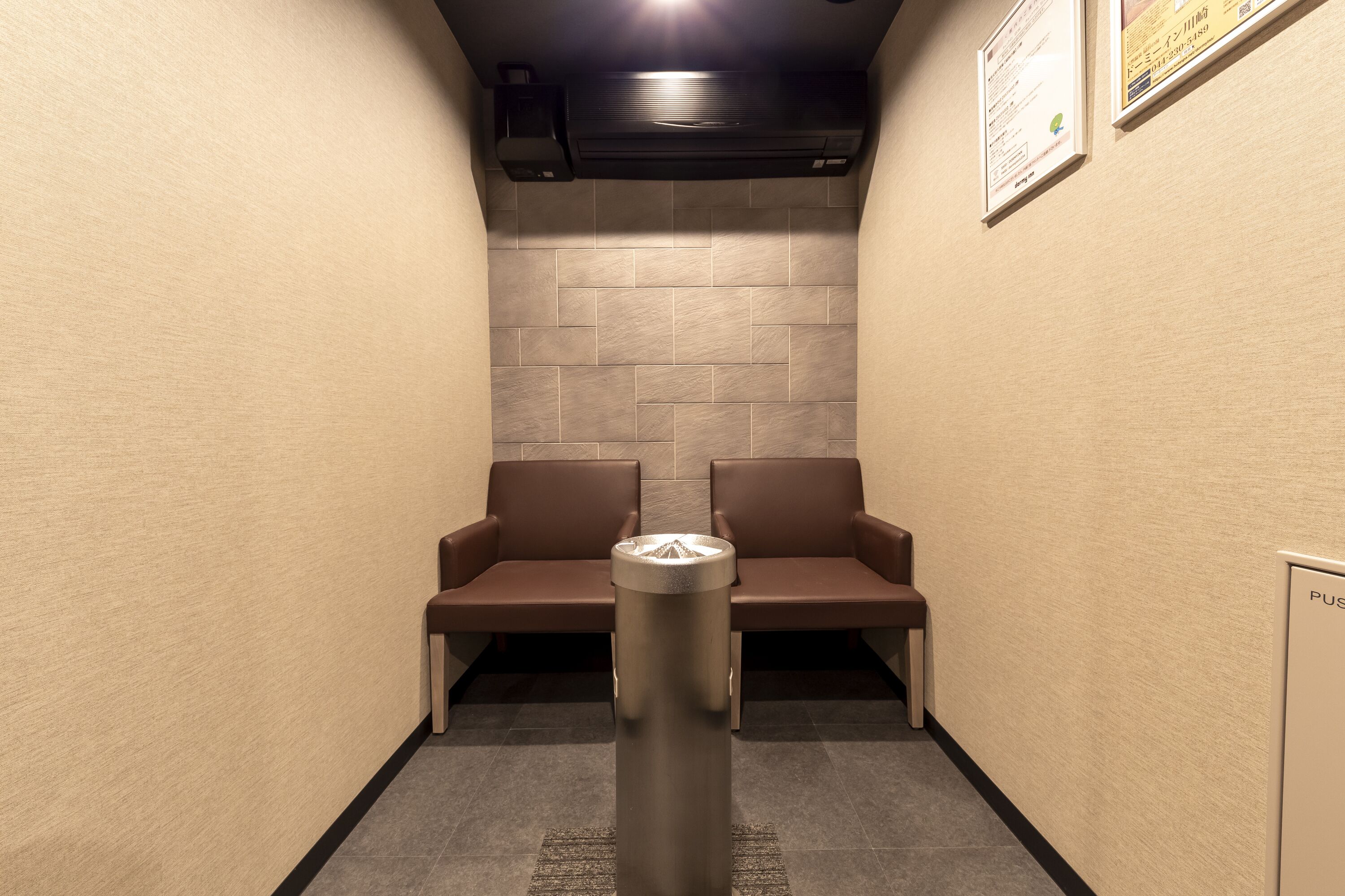 A narrow hallway with two brown cushioned seating areas and a metallic pillar in the center.