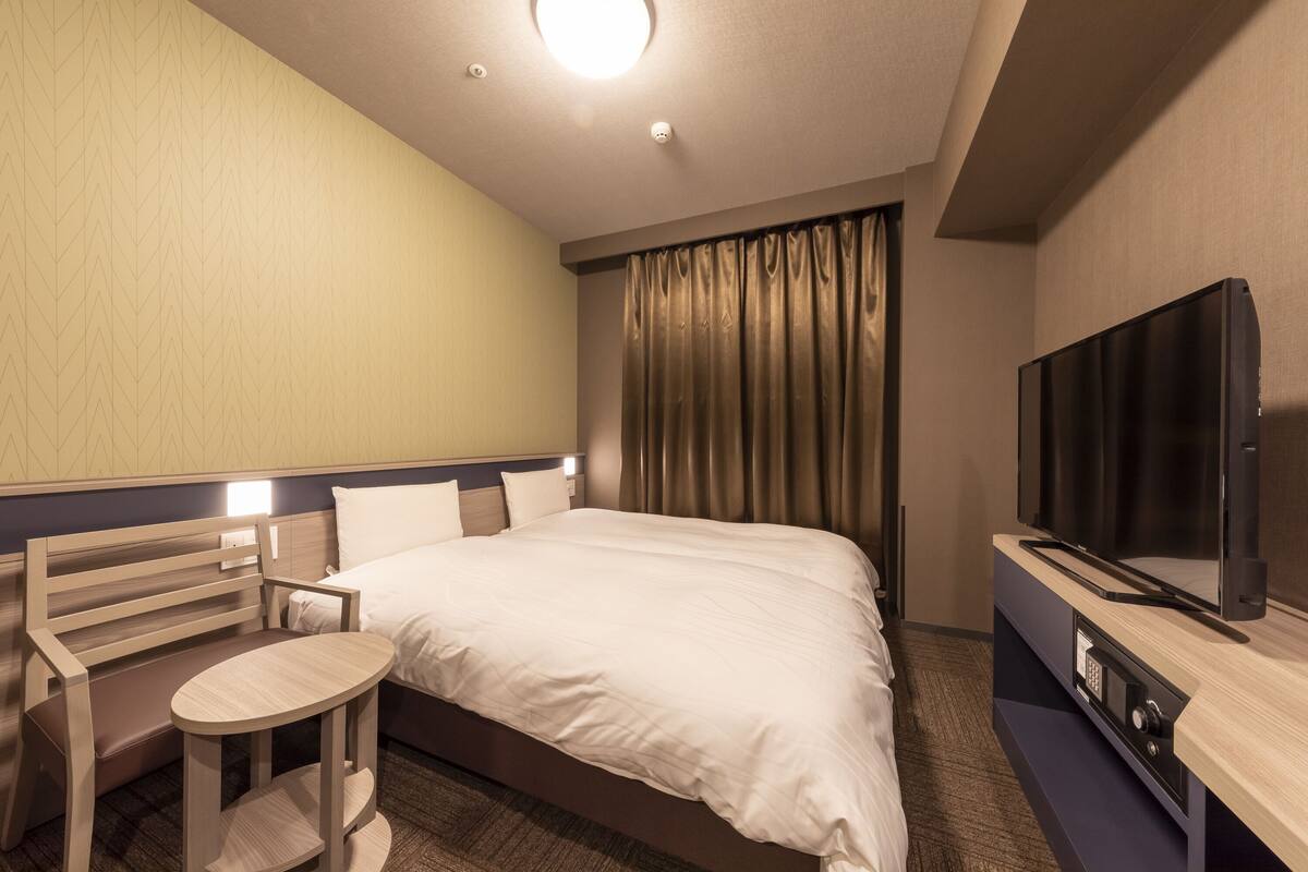 A hotel room with a bed, a TV, a desk, and a chair.
