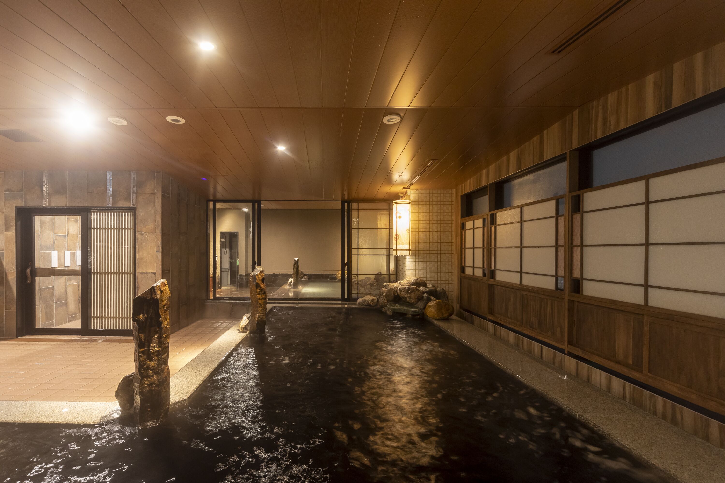 Un onsen japonés tradicional con interiores de madera, zona de aguas termales y una sala con esteras de tatami.