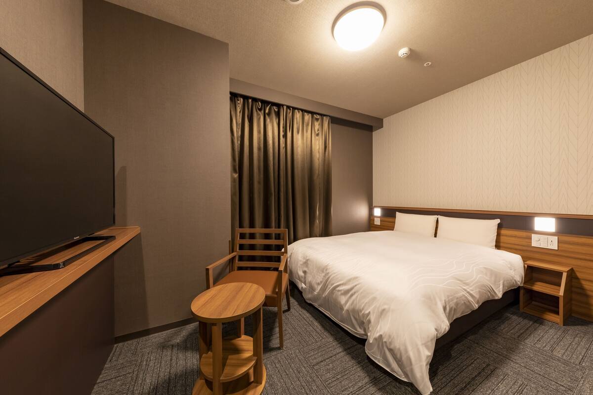 A hotel room with a bed, a desk, a chair, a TV, and a curtain.