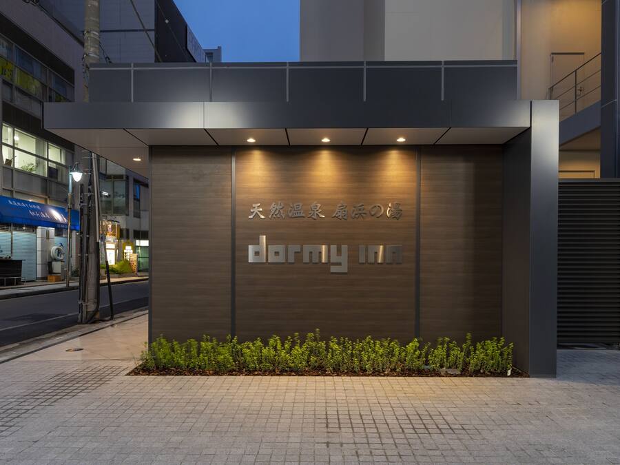 Um edifício moderno com uma placa indicando "dormy inn" e uma pequena área de jardim na frente.
