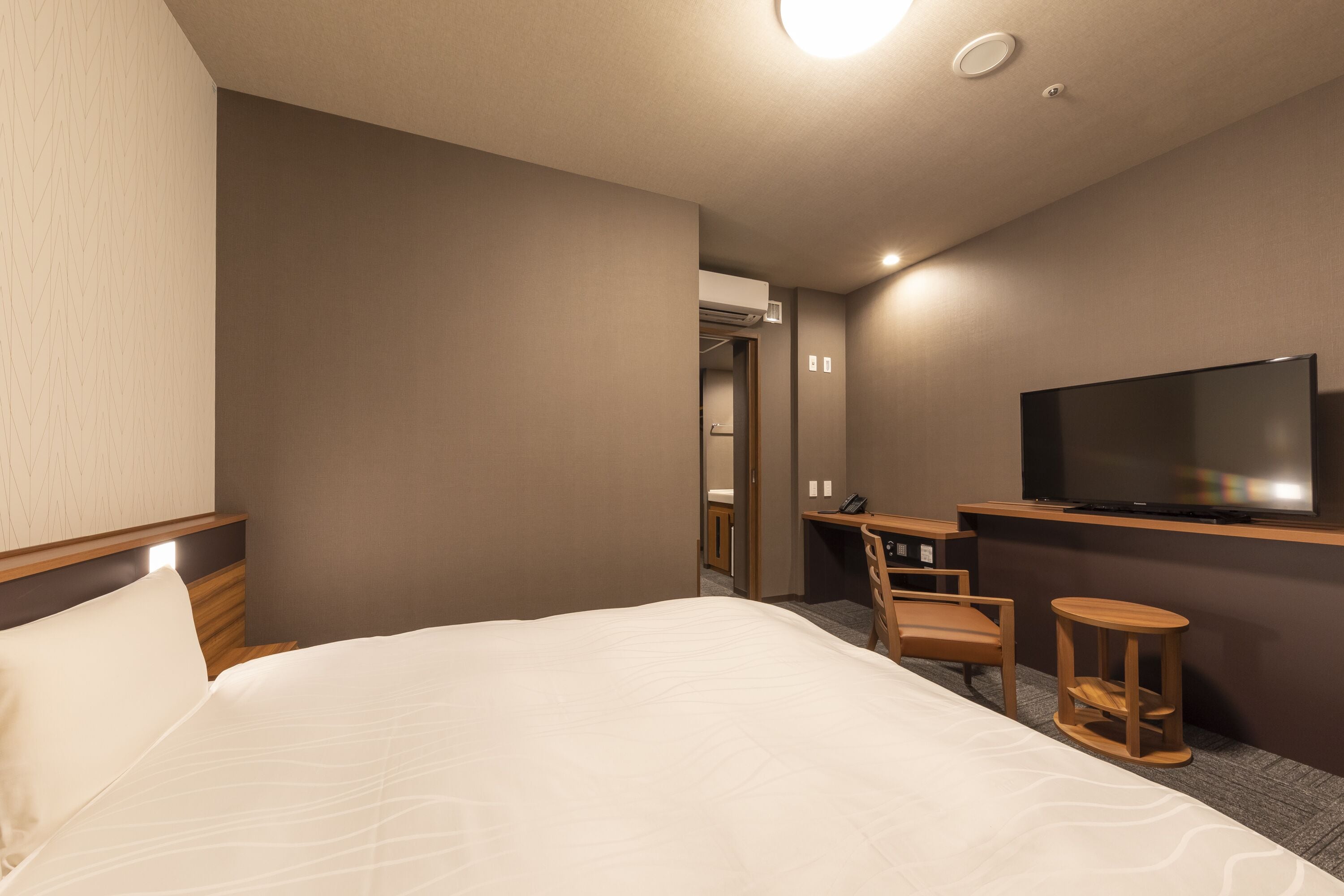 A hotel room with a large bed, a desk with a chair, a television, and a small table.