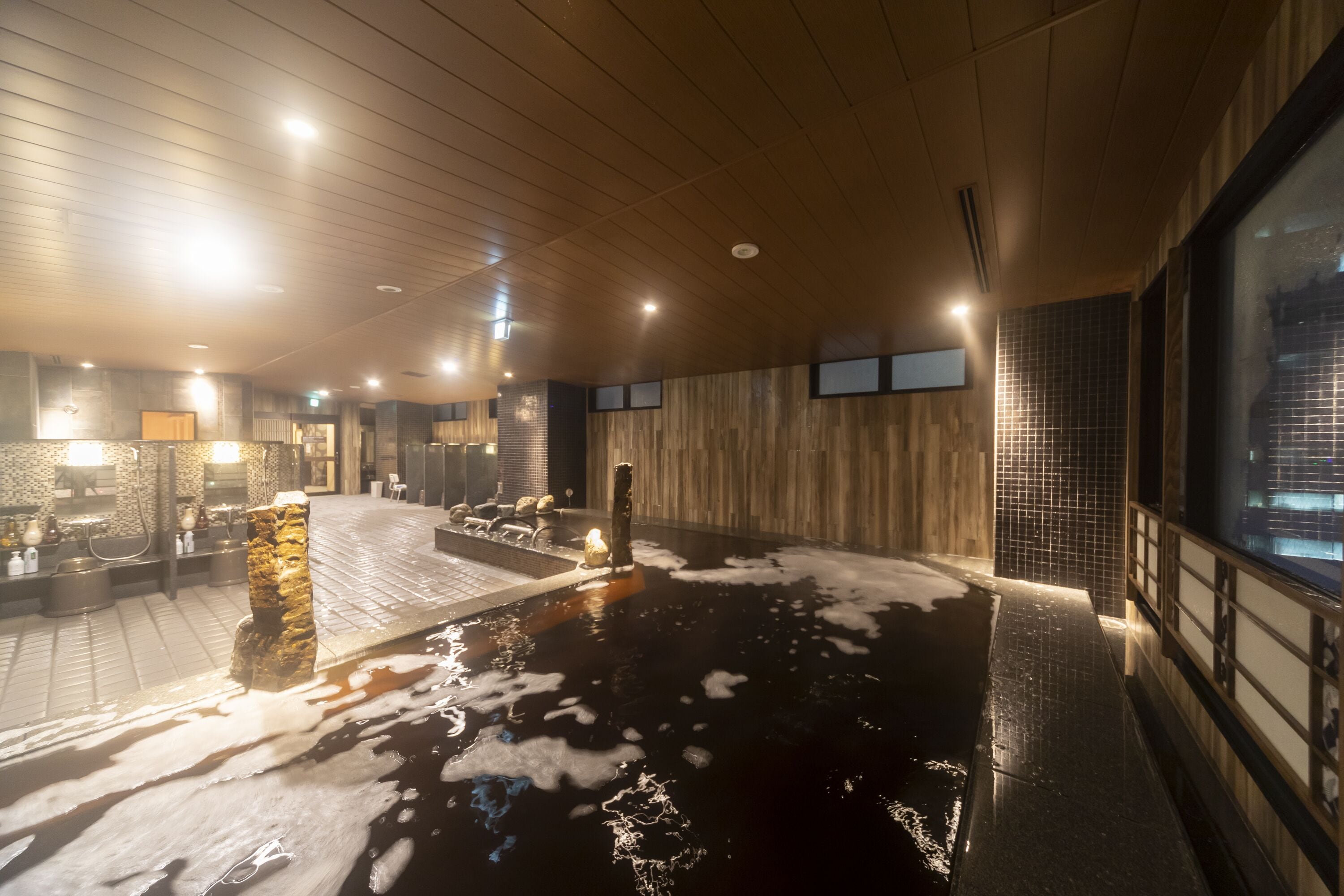 A spa area with a large hot tub, wooden ceiling, and tiled walls.