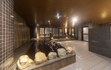 A modern indoor spa with a heated stone bath, wooden walls, and large windows.