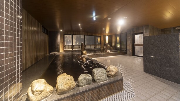 A modern indoor spa with a heated stone bath, wooden walls, and large windows. - Dormy Inn Kawasaki Natural Hot Spring (Kawasaki)