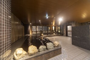 Un spa moderno en el interior con una bañera de piedra climatizada, paredes de madera y ventanas amplias.