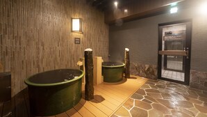 A spa area with two large tubs, a wooden wall, a stone floor, and a door with a sign. - Dormy Inn Kawasaki Natural Hot Spring (Kawasaki)