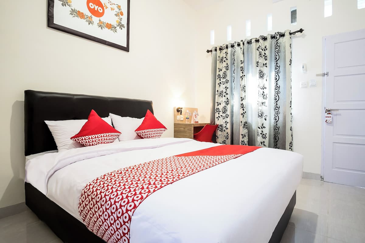 Un lit bien fait, avec une couvre-lit à motifs, une tête de lit noire et des oreillers rouges.