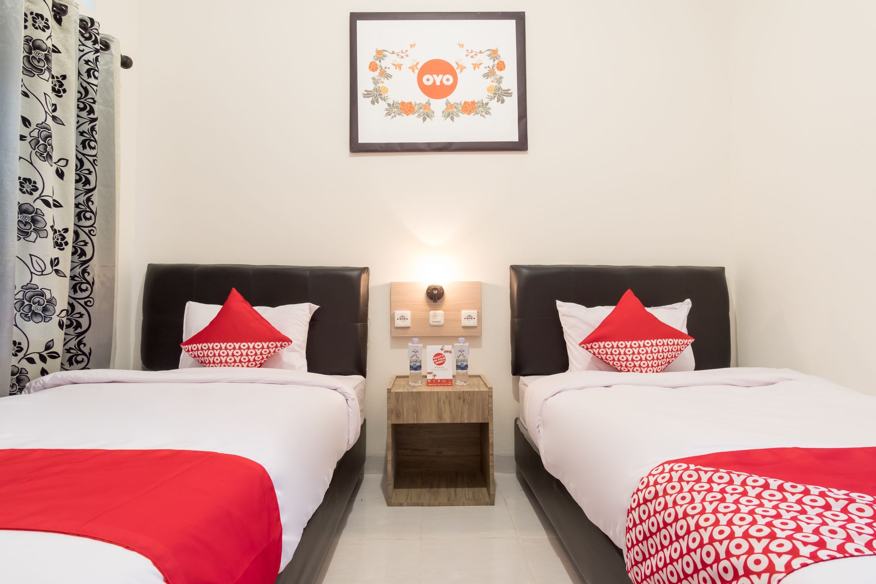 A hotel room with two beds, each with a red and white bedspread, a wooden nightstand with a lamp, and a framed picture on the wall.