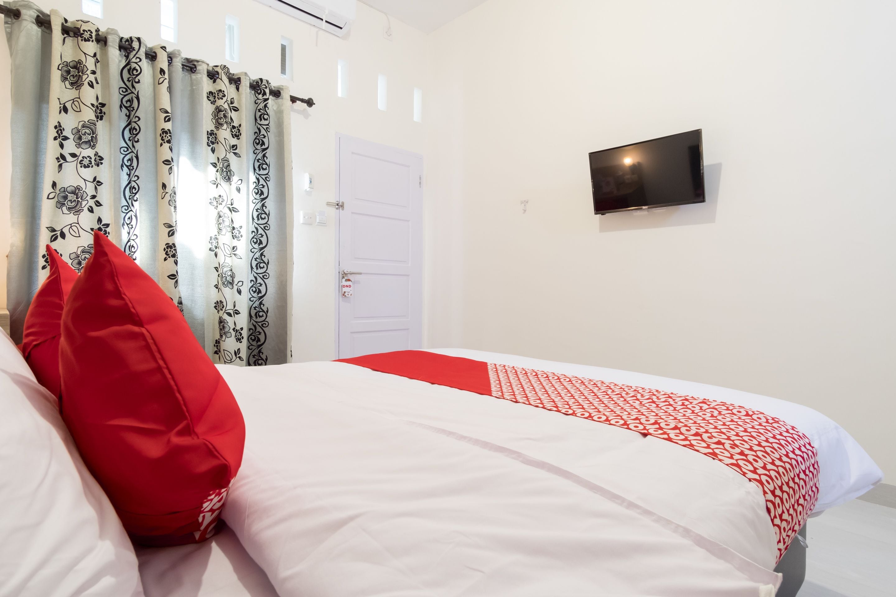 A bedroom with a bed, red and white bedding, a television on the wall, and a door with a lock.