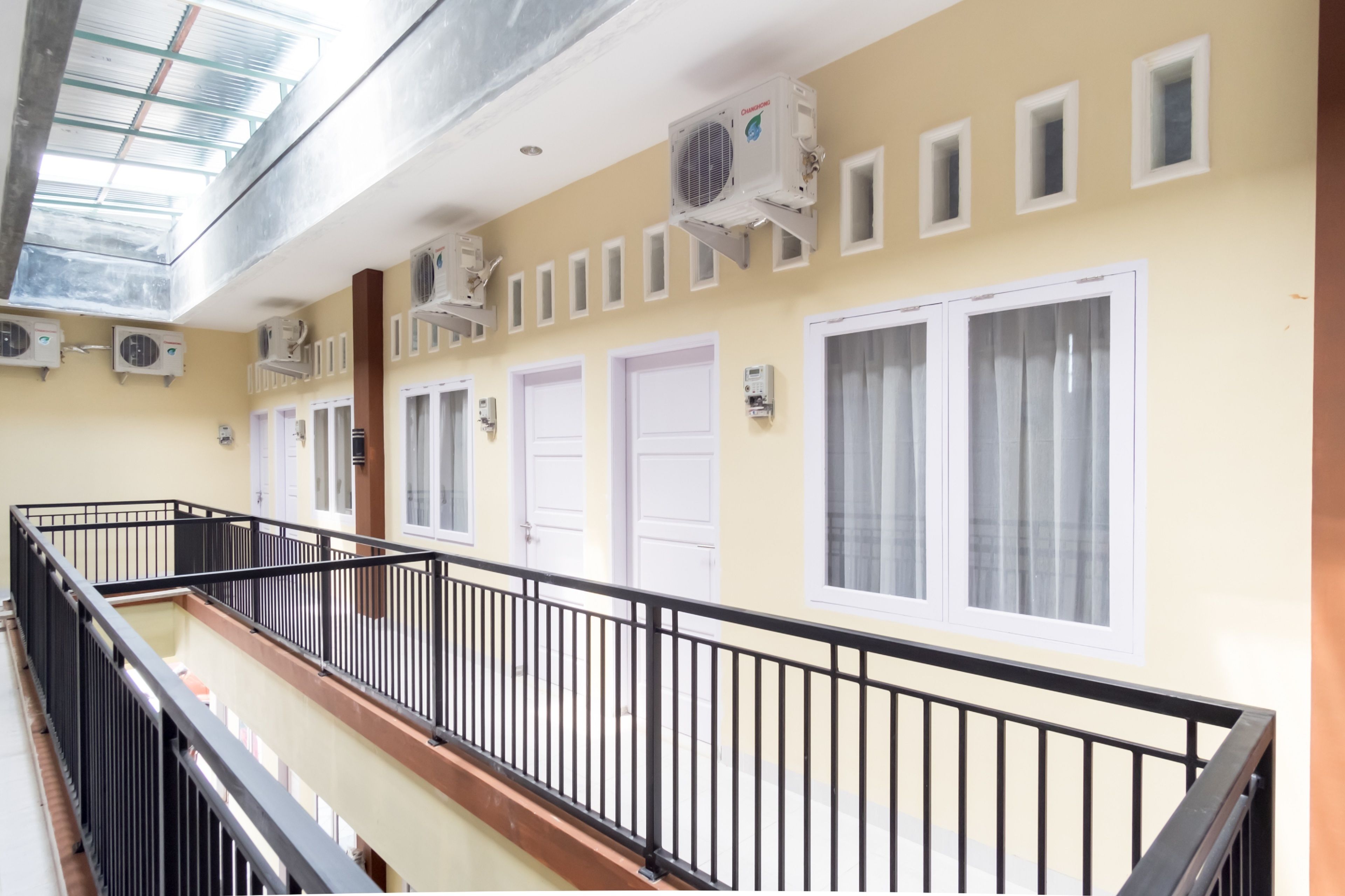 Un couloir avec une rambarde noire, des unités de climatisation et des portes équipées de rideaux.