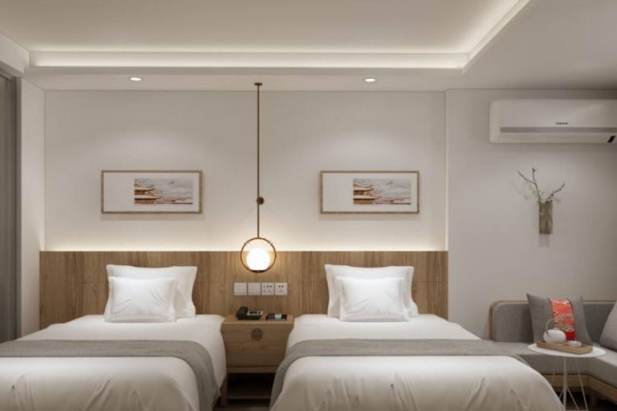 Une chambre d’hôtel moderne avec deux lits, une table de chevet avec une lampe, une petite table d’appoint avec un vase et un appareil de climatisation fixé au mur.